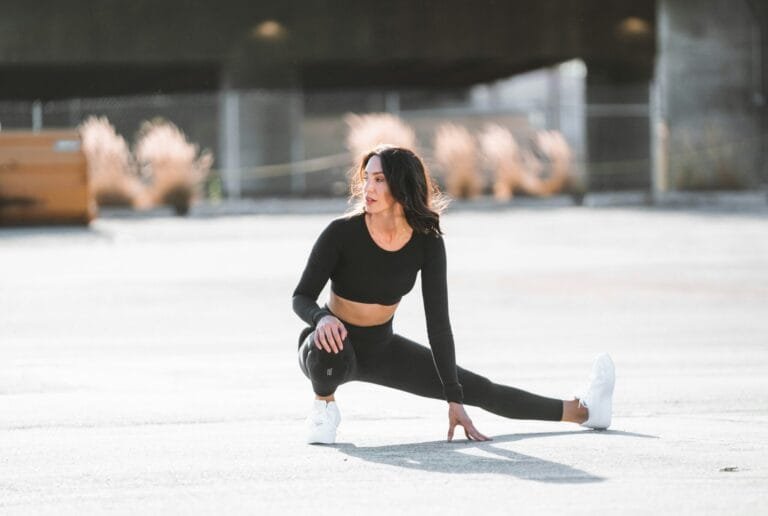 Woman stretching in a black long-sleeve crop top and black leggings on an outdoor court