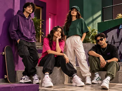 Four friends in streetwear sitting and standing on steps with a skateboard